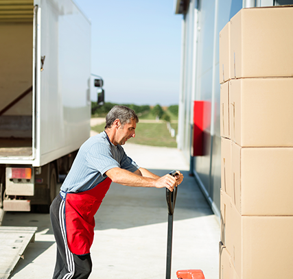 A man in an apron moving a hand-truck stacked with packages.