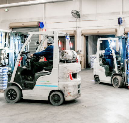The interior of a warehouse with two forklifts driving around.